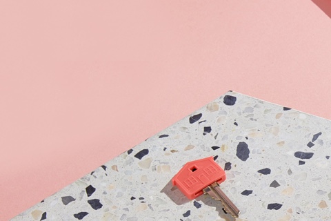 Coral-pink house key resting on terrazzo against a soft pink backdrop — minimalist 'flip card' lifestyle image, pink brand-color set.